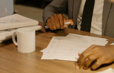 Free Close-up of a businessman holding and reviewing documents on a wooden desk. Stock Photo